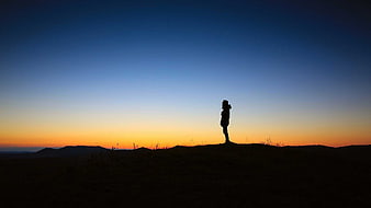 Silhouette of woman standing on hill at sunset