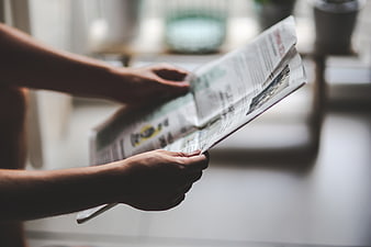 Close-up of hands holding and reading a newspaper