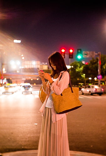 Woman checking smartphone at city street intersection at night