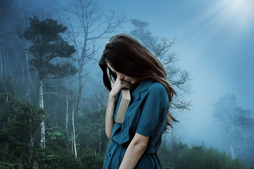 Sad woman holding book in misty blue forest