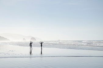 Surfers walking on misty beach with surfboards