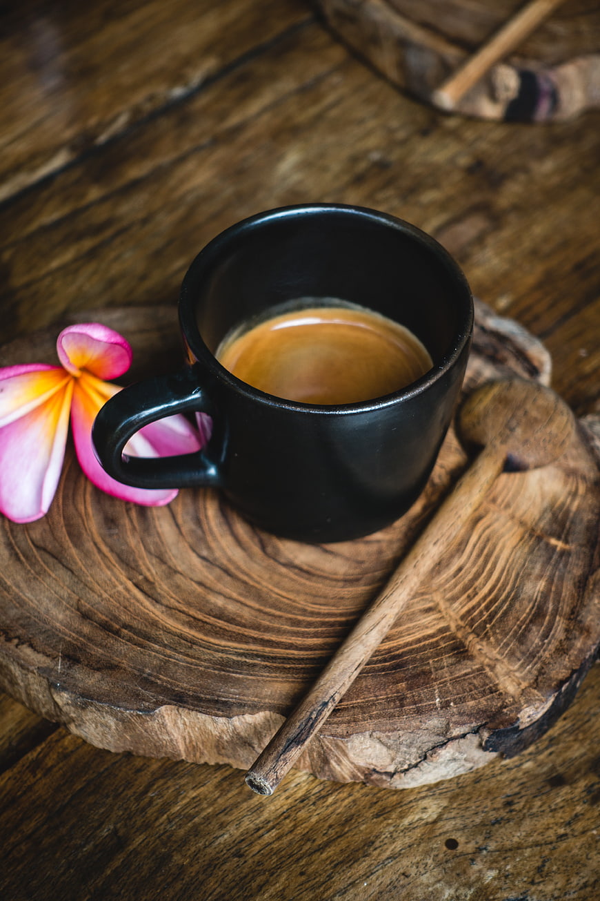 Black cup of espresso on rustic wooden board with flower