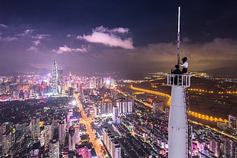 Couple on tower overlooking vibrant city skyline at night