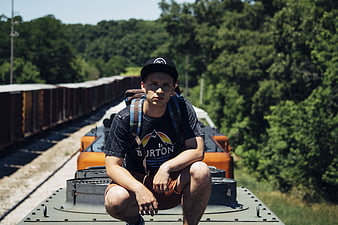 Young Man Squatting on Freight Train Roof in Forest