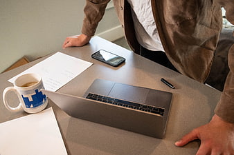 Man standing at desk with laptop, coffee, and documents