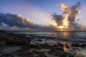 Dramatic Sunset Over Rocky Ocean Coastline with Golden Clouds