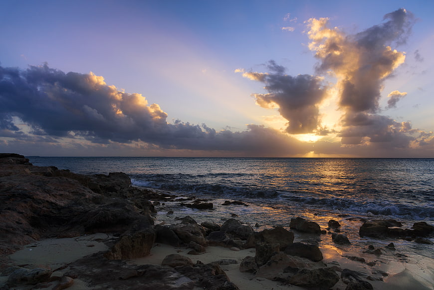 Dramatic Sunset Over Rocky Ocean Coastline with Golden Clouds