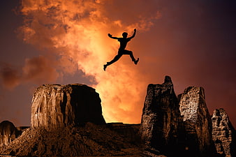Silhouette of man jumping between rock formations at sunset