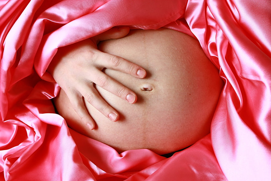 Close-up of pregnant belly with hand on pink satin fabric