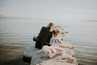 Mother and daughter sitting on rocks by the sea