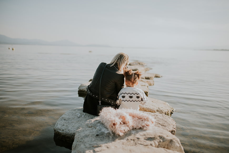 Mother and daughter sitting on rocks by the sea