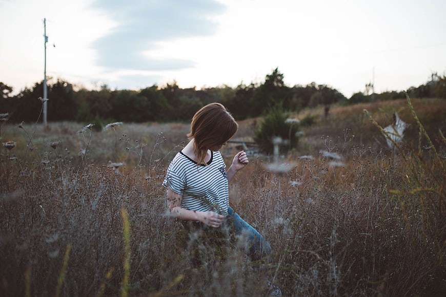 Woman in striped shirt walking through tall dry grass field