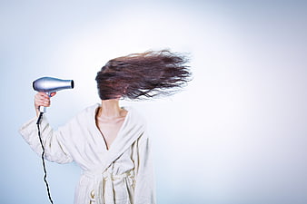 Woman in white robe drying hair with blow dryer