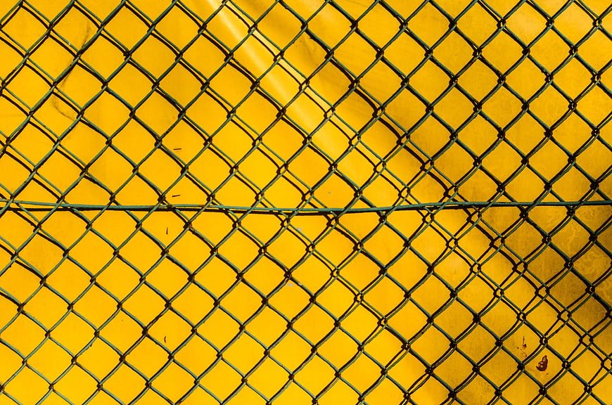 Green Chainlink Fence Against Vibrant Yellow Wall Background