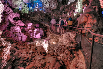 Tourists walking on a path through a colorful illuminated cave