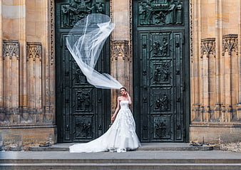 Bride in White Gown with Flowing Veil Before Gothic Cathedral Doors
