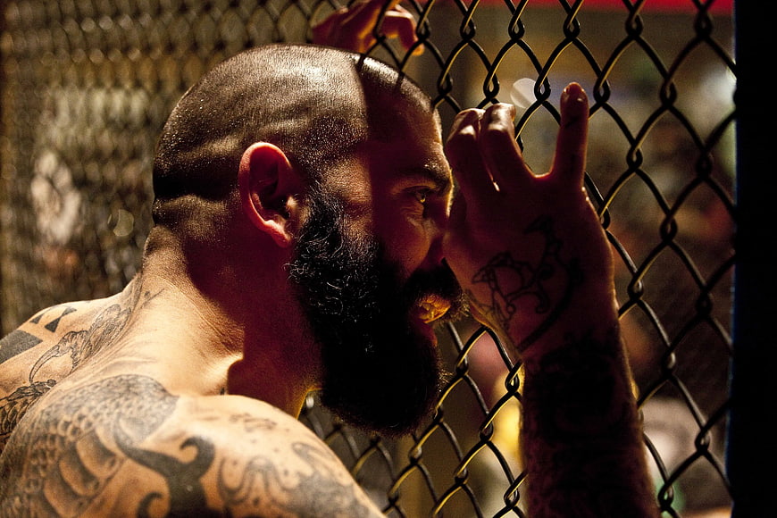 Tattooed Fighter Leaning on MMA Cage Fence