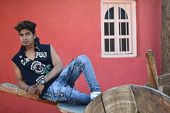 Young man in sleeveless hoodie posing against red wall