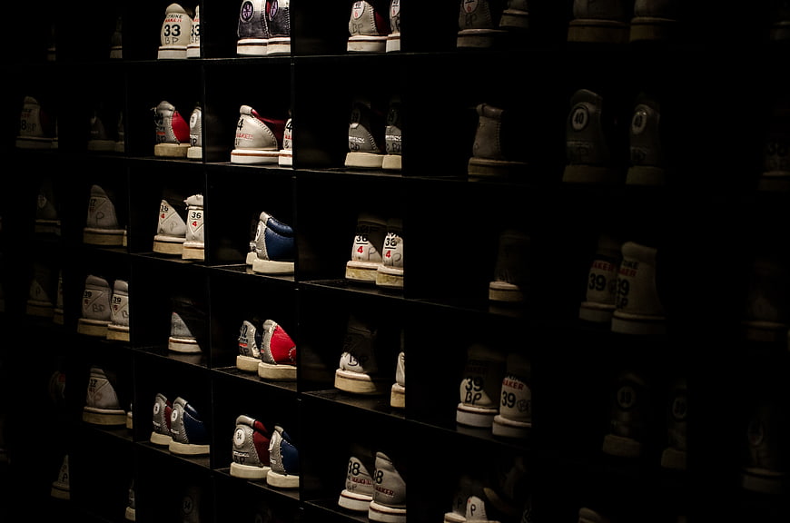 Rows of bowling shoes on dark shelves in a dimly lit alley