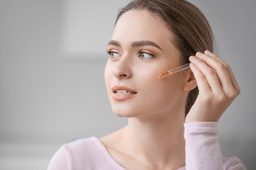 Young woman applying serum dropper to face skincare