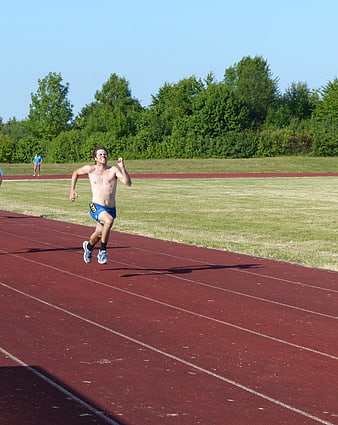 Shirtless male sprinter running on red track