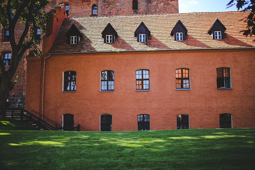 Red brick castle wall with dormer windows and green lawn