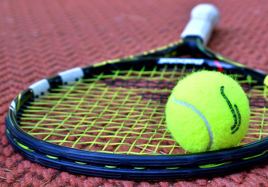 Tennis racket and ball on red clay court surface