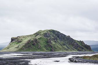 Green Rocky Hill on Coastal Shoreline Under Overcast Sky