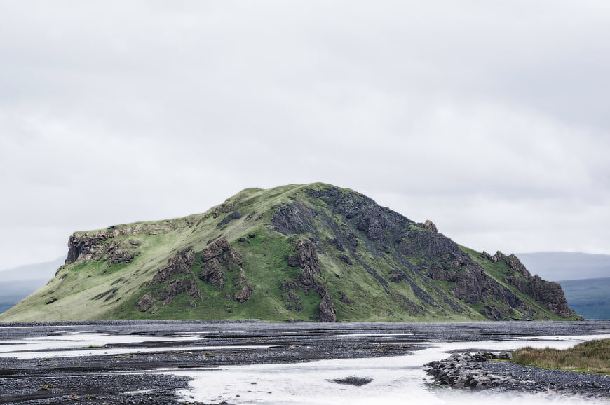 Green Rocky Hill on Coastal Shoreline Under Overcast Sky