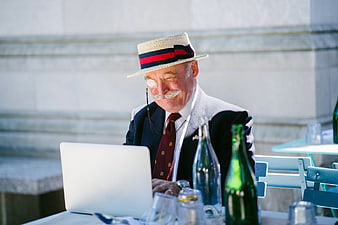 Senior man with monocle and straw hat using laptop at cafe
