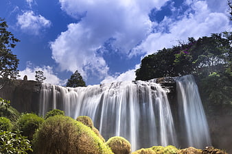 Wide Angle View Of A Large Waterfall Flowing Under A Blue Sky