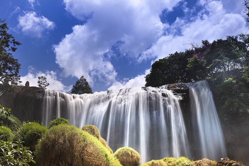 Wide Angle View Of A Large Waterfall Flowing Under A Blue Sky