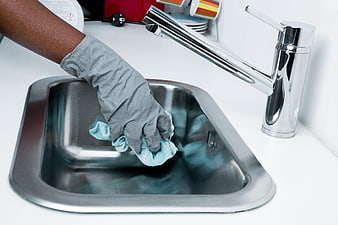 Hand in rubber glove cleaning stainless steel kitchen sink