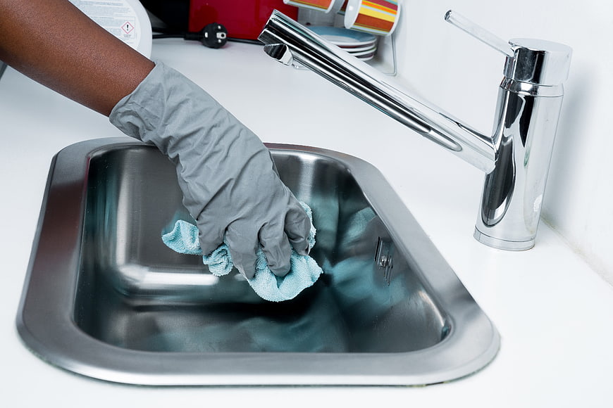 Hand in rubber glove cleaning stainless steel kitchen sink