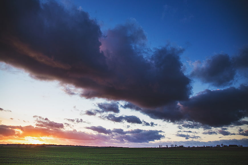 Dramatic sunset over green field with dark storm clouds