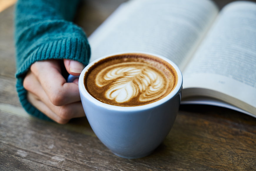 Cozy Latte Art Coffee Cup With Book And Hands On Wooden Table