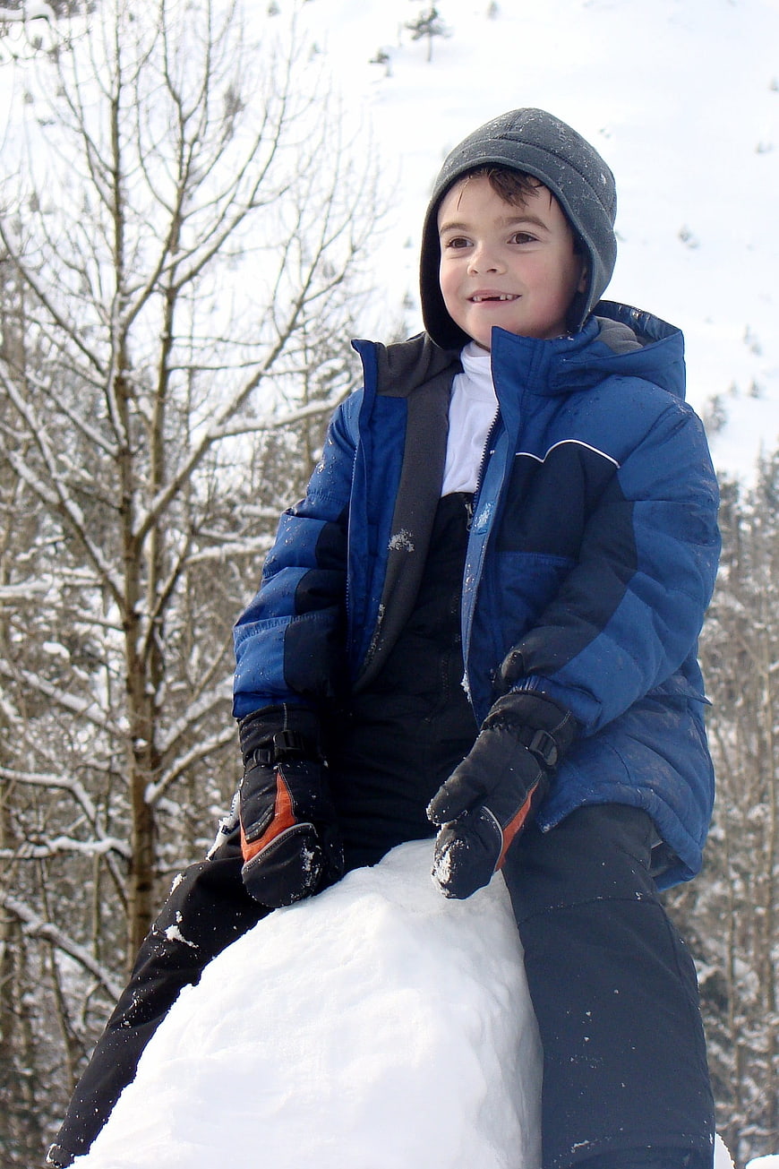 Happy Boy Sitting on Snow Mound in Winter