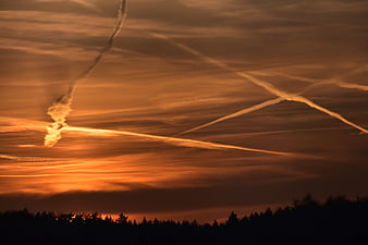 Dramatic orange sunset sky with intersecting airplane contrails