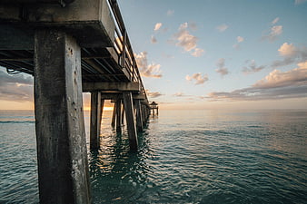 Concrete pier extending over calm ocean at sunset