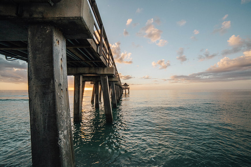 Concrete pier extending over calm ocean at sunset