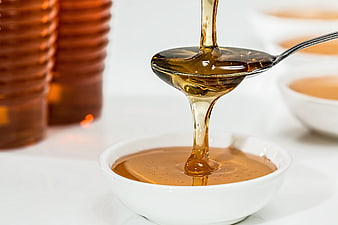 Golden Honey Pouring from Spoon into White Bowl