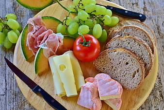 Rustic charcuterie board with melon, prosciutto, cheese, grapes, tomato, and bread