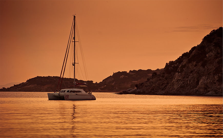 Catamaran sailing at sunset on calm orange sea