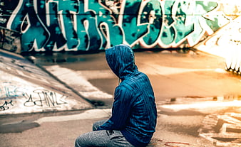 Person in Blue Hoodie Sitting in Graffiti Skate Park