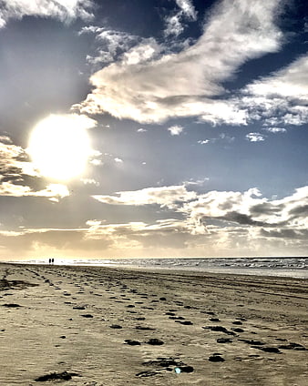 Silhouetted Couple Walking on Sandy Beach with Dramatic Clouds