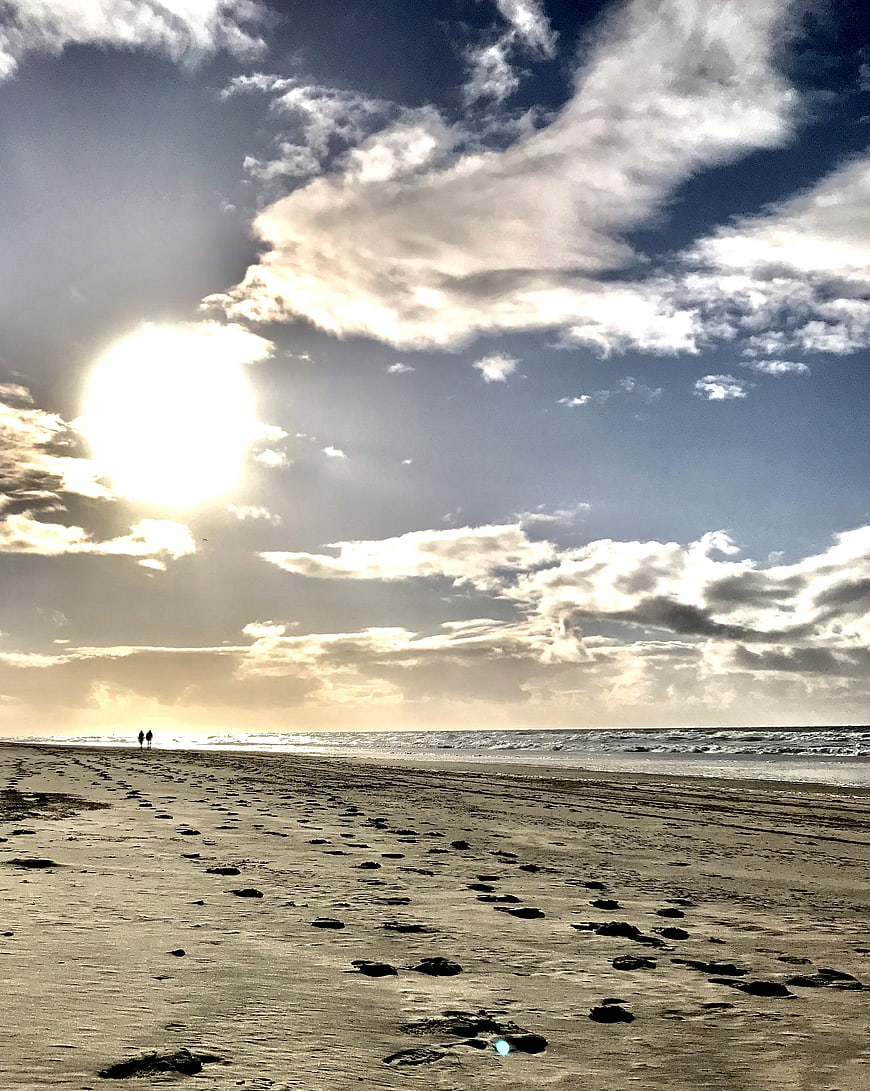 Silhouetted Couple Walking on Sandy Beach with Dramatic Clouds