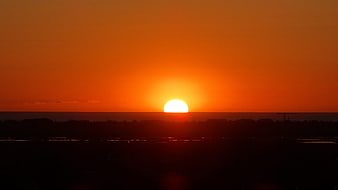 Vibrant Orange Sunrise Over Dark Silhouetted Horizon