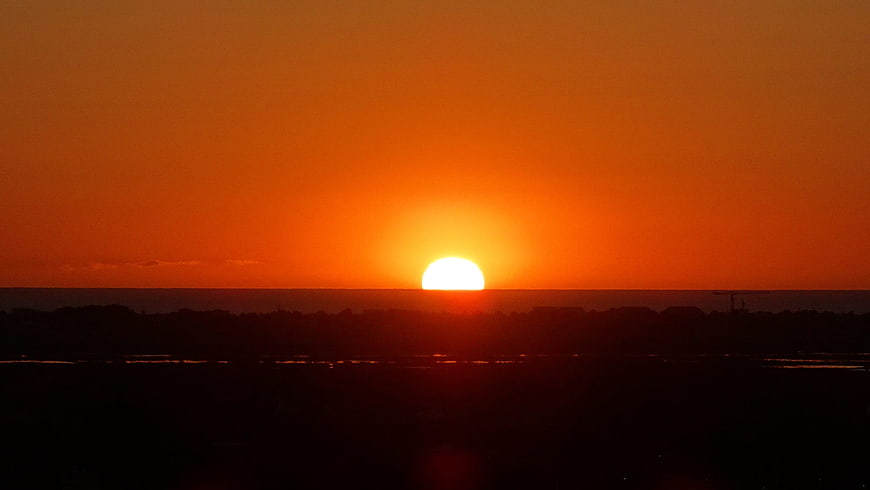 Vibrant Orange Sunrise Over Dark Silhouetted Horizon