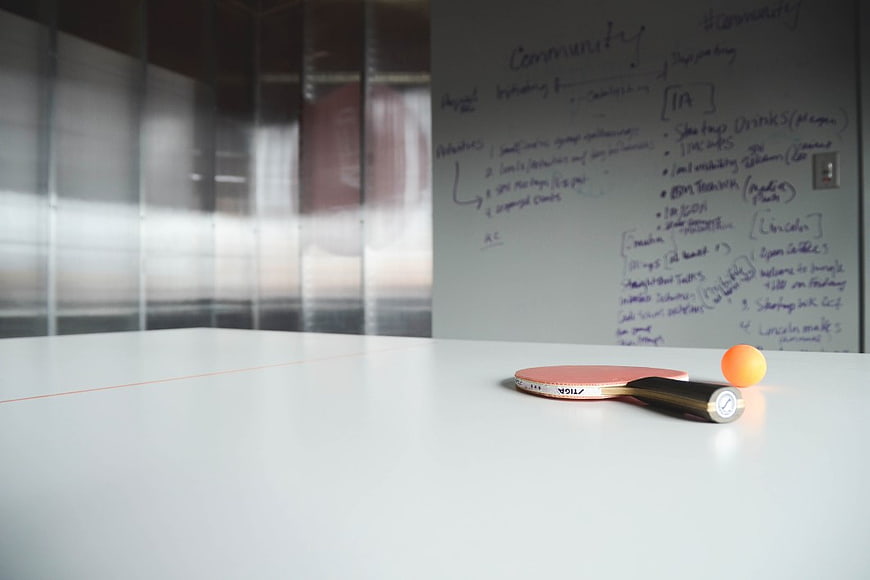 Ping Pong Paddle and Ball on White Table with Whiteboard