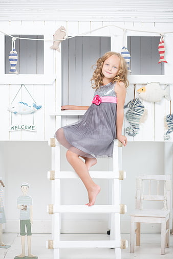 Young girl in grey dress sitting on white ladder in nautical themed room